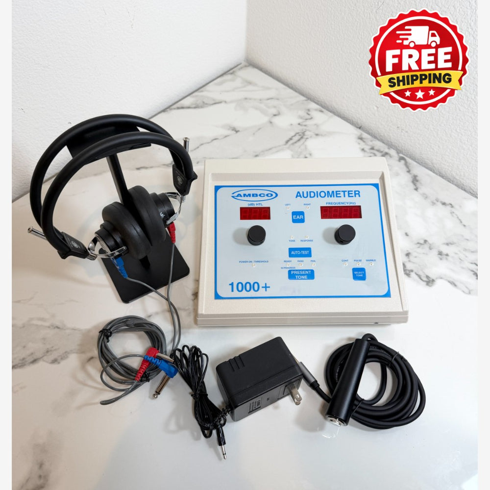 A portable audiometer testing device with a beige control panel, blue markings, black headphones on a stand, test leads, and a power adapter, arranged on a white marble-patterned surface against a white wall. A red 'FREE SHIPPING' badge is in the top right corner.