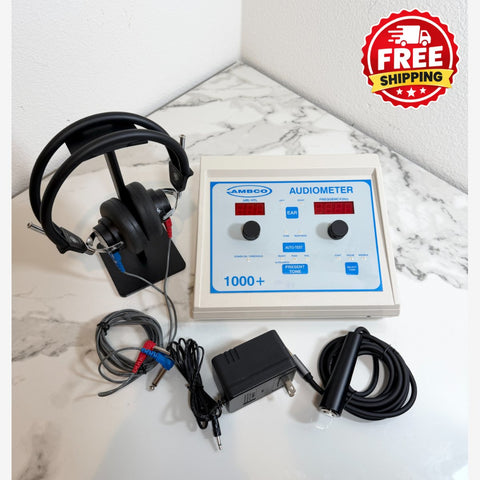 A portable audiometer testing device with a beige control panel, blue markings, black headphones on a stand, test leads, and a power adapter, arranged on a white marble-patterned surface against a white wall. A red 'FREE SHIPPING' badge is in the top right corner.