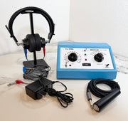 An AMBCO 650A Audiometer with a blue control box, black headphones on a stand, a black power adapter, and a black cable with a silver and black electrode, arranged on a light marble surface against a white wall.