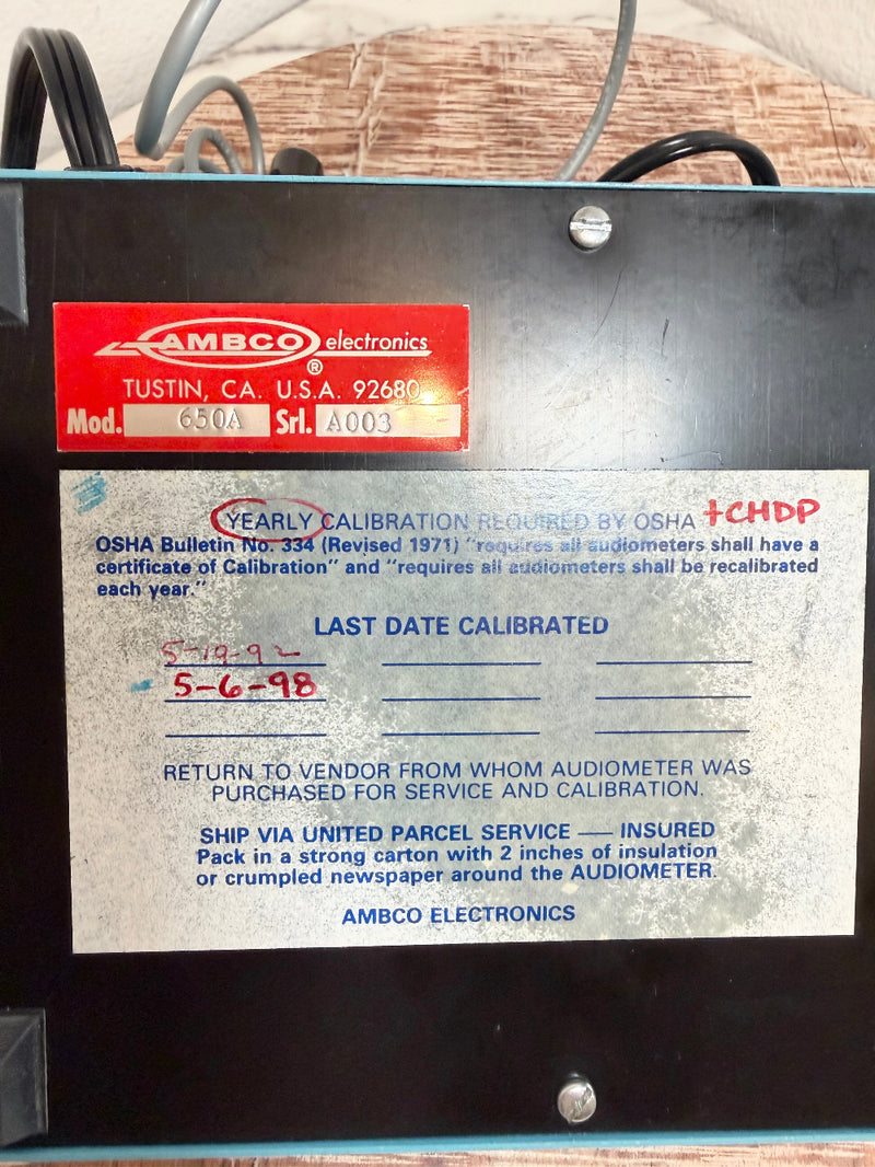 An AMBCO 650A audiometer device control unit with a black metal casing, featuring a red manufacturer label and a white OSHA compliance sticker on the front.