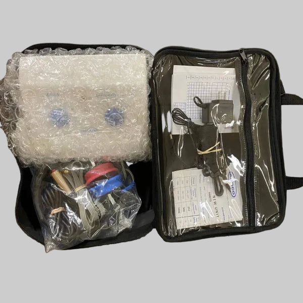 An open black zippered carrying case for Ambco 650AB audiometer shown on a gray surface, with bubble wrap and accessories inside on the left and a clear front pocket containing papers, cords, and a small device on the right.