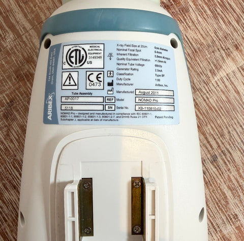 Close-up of Aribex Nomad Pro Handheld Dental Intraoral System with certification labels on a wooden surface
