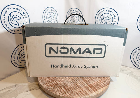 Nomad handheld X-ray system packaging on a wooden surface with branded background.