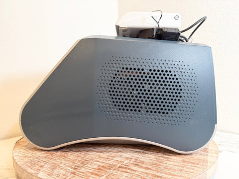 A gray BioLite Ceralas laser device with a perforated front grille, resting on a round wooden slice against a light beige wall.