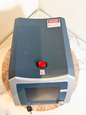 A BBioLite Ceralas laser device, resting on a round wooden coaster on a marble surface.