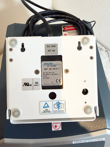 A Steute KF 11W60 RF amplifier power supply enclosure with a white metal backplate, black cable, and various certification stickers, shown on top of a dark gray Ceralas machine.