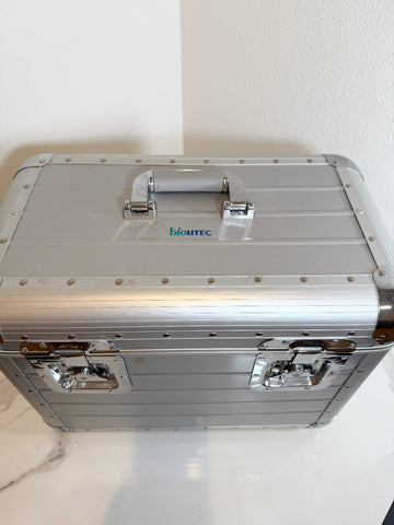 A silver aluminum hard case with a top handle, latches, and rivets, featuring the 'biotech' logo printed on the lid, set against a plain off-white background.