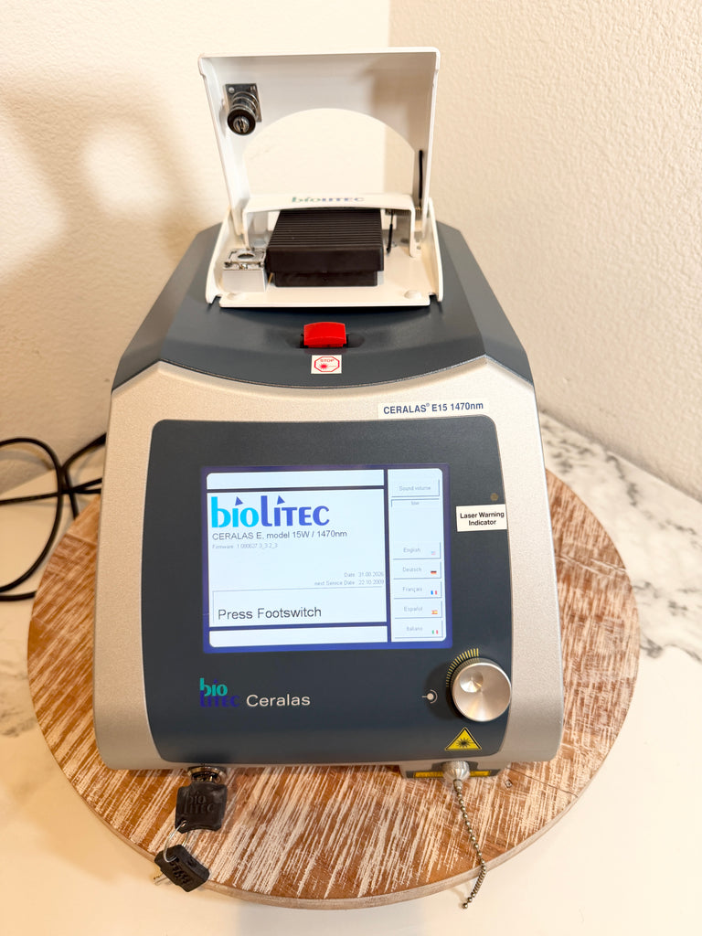 A BBioLite Ceralas laser device with a gray and silver body, a digital screen, and a white hinged lid on top, resting on a round wooden tray.