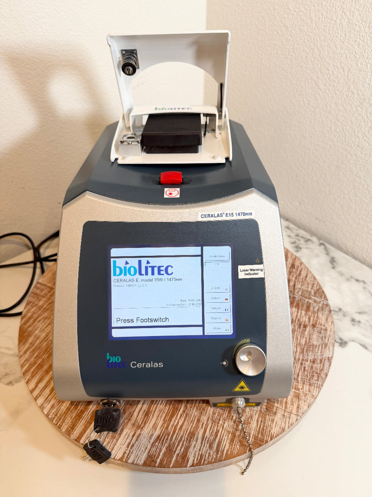 BioLite Ceralas laser device with a digital screen and open top lid, sitting on a round wooden stand against a beige wall.