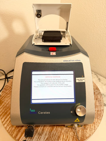 A BioLite Ceralas laser device with a gray and silver body, a digital control screen, and an open lid on top, sitting on a round woven mat.
