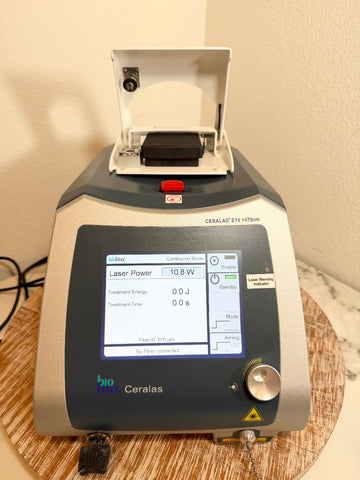 A BioLite Ceralas laser device with its lid open, sitting on a round wooden tray against a beige wall.