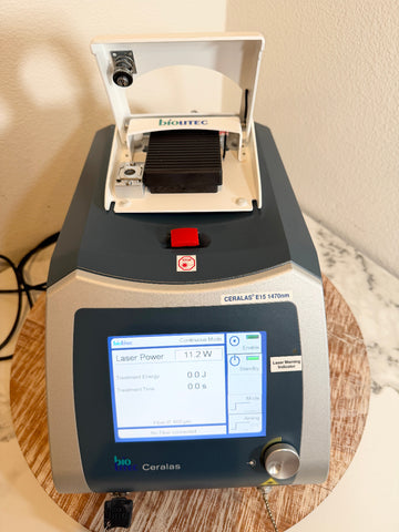 A BioLite Ceralas laser device with its lid open, showing a digital screen on a wooden stand against a beige wall.