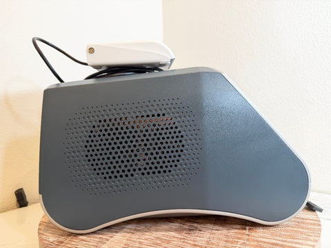 A gray BioLite Ceralas laser device with a perforated front grille and a white top attachment, resting on a wooden surface against a beige wall.