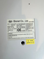 Close-up of the back of a Bionet medical CardioCare cardiac device showing a product information label, model details, CE markings, and a yellow QC PASS sticker on a light gray surface.