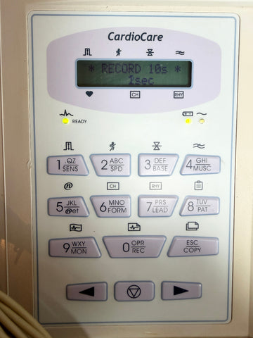 A close-up of a CardioCare electronic device control panel with a small display screen and multiple labeled buttons, photographed against a light neutral background.