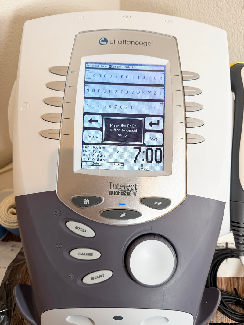 A Chattanooga Intelect Legend XT 2760 device with a beige and dark gray plastic body, featuring a digital screen and control buttons, shown in a home setting.