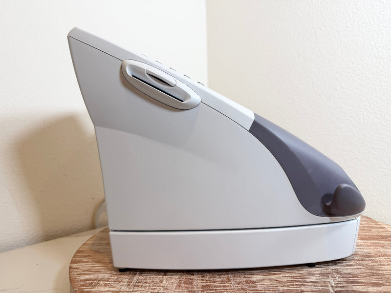 A white and dark gray Chattanooga Intelect Legend XT 2760 device, shown from a side angle on a wooden surface against a beige wall.