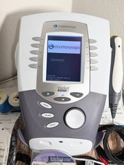 A Chattanooga Intelect Legend XT 2760 device with its touchscreen display active, shown alongside a pen-like tool and cables on a tabletop.
