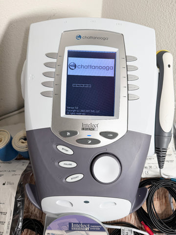A Chattanooga Intelect Legend XT 2760 device with its touchscreen display active, shown alongside a pen-like tool and cables on a tabletop.