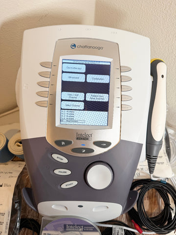 A CChattanooga Intelect Legend XT 2760 device with its handheld wand, shown on a desk with paperwork in the background.