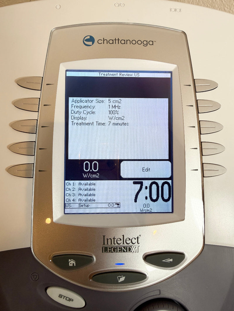 A close-up of a Chattanooga Intelect Legend XT 2760 device with a silver and dark gray plastic body, featuring a color screen displaying treatment settings and a STOP button below the screen.