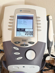 A Chattanooga Intelect Legend XT 2760 device with its treatment wand, shown on a wooden surface with a beige wall in the background.