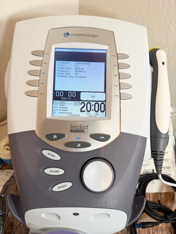 A Chattanooga Intelect Legend XT 2760 device with its treatment wand, shown on a wooden surface with a beige wall in the background.