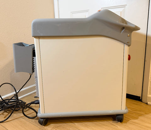 Sideview of a Cynosure Smartlip laser system with a side-mounted gray attachment and black power cords,