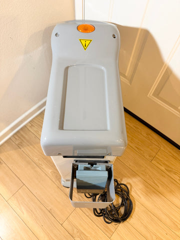 A Cynosure Smartlip laser system with its power cord extended, standing on a light wood floor against a beige wall.