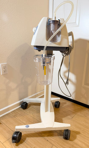 A Medela Dominant 50 Suction/Aspiration System on a wheeled stand, photographed indoors on a wood floor against a beige wall and white door.