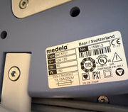 A close-up of a Medela Dominant 50 Suction/Aspiration System label sticker on a gray plastic surface, showing product details, barcodes, certification marks, and text including 'medela' and 'Baar / Switzerland'.