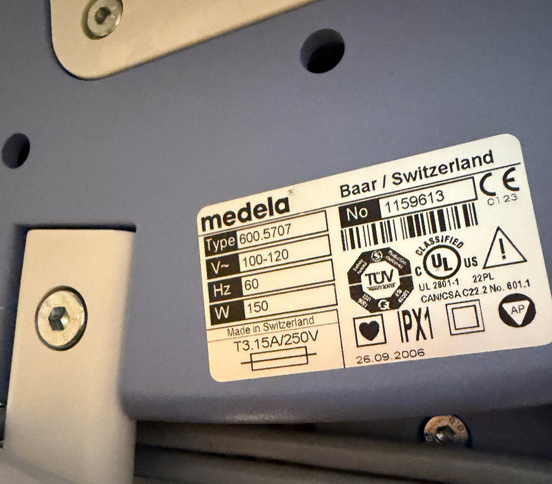 A close-up of a Medela Dominant 50 Suction/Aspiration System label sticker on a gray plastic surface, showing product details, barcodes, certification marks, and text including 'medela' and 'Baar / Switzerland'.