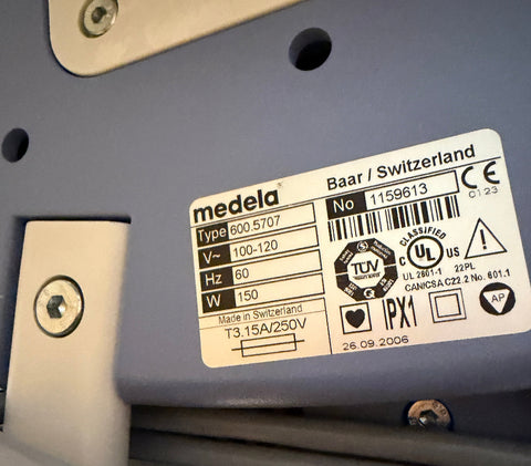 A close-up of a Medela Dominant 50 Suction/Aspiration System label sticker on a gray plastic surface, showing product details, barcodes, certification marks, and text including 'medela' and 'Baar / Switzerland'.