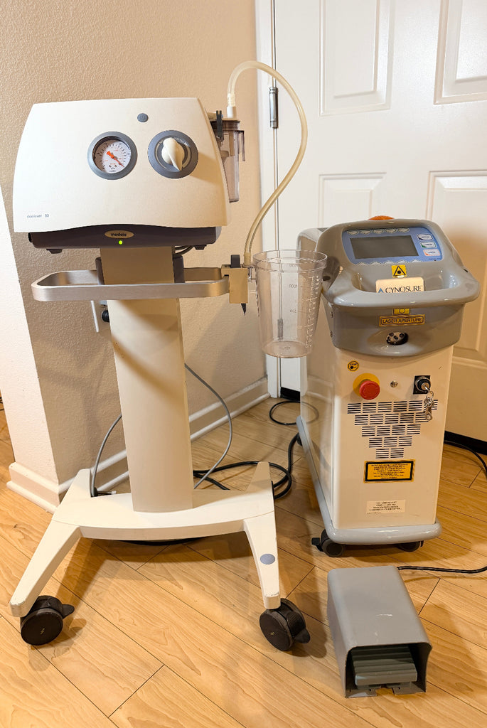 A Cynosure SmartLipo Laser System and Medela Dominant 50 Suction/Aspiration System set on a wood floor in front of a white door. 