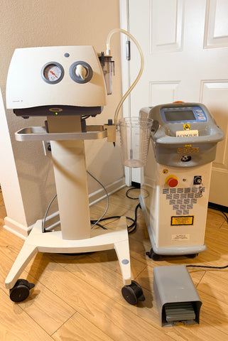 A Cynosure SmartLipo Laser System and Medela Dominant 50 Suction/Aspiration System set on a wood floor in front of a white door. 