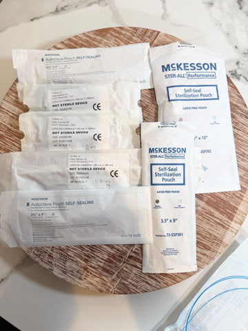 Several packaged medical sealing and sterilization pouches from Mckesson and Autoclave Pouch are arranged on a round wooden tray over a white marble surface.