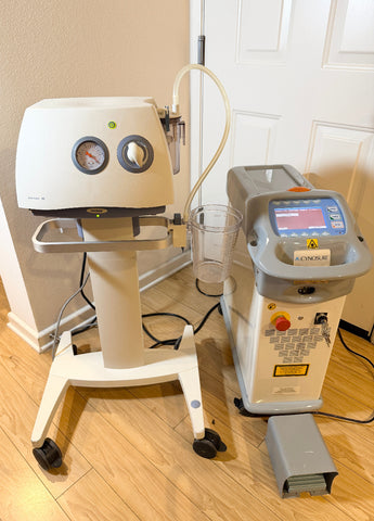 A Cynosure SmartLipo Laser System and Medela Dominant 50 Suction/Aspiration System set on a wood floor in front of a white door. 