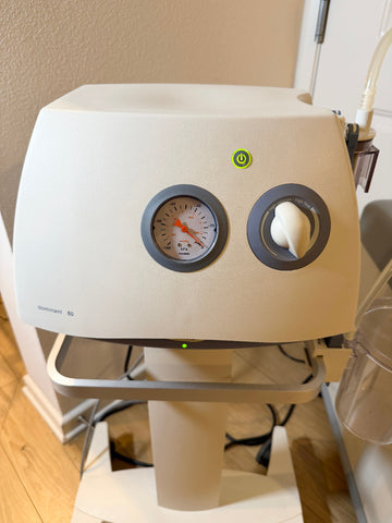 A Medela Dominant 50 Suction/Aspiration System with a pressure gauge, rotary control knob, green power indicator light, and a clear handpiece attached, photographed indoors on a stand.