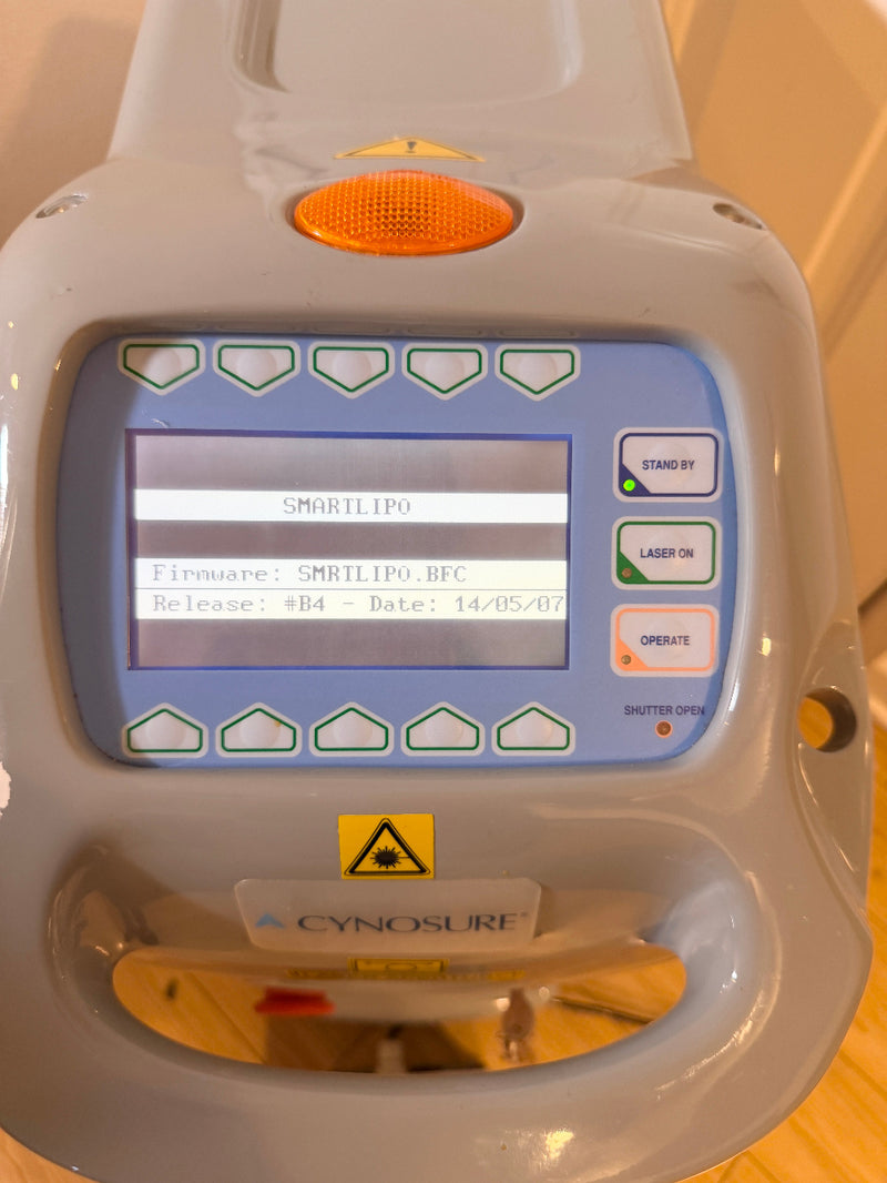 A close-up of a Cynosure SMRTLIP0 laser lipolig device with a gray plastic casing, a blue control panel, and a screen displaying system text.