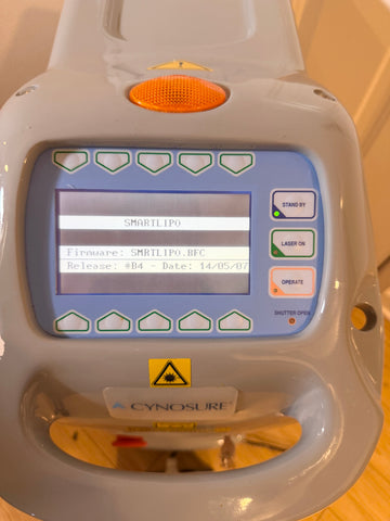 A close-up of a Cynosure SMRTLIP0 laser lipolig device with a gray plastic casing, a blue control panel, and a screen displaying system text.