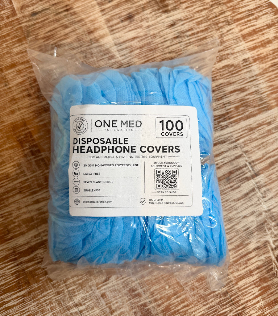 A package of One Med Calibration disposable headphone covers in light blue, sealed in a clear plastic bag with a white product label, placed on a wooden surface.