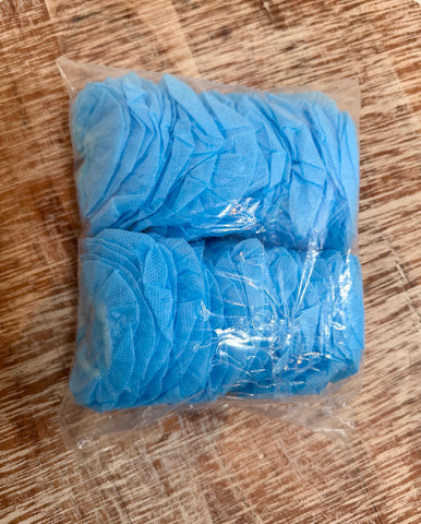 A clear plastic bag containing multiple light blue disposable non-woven fabric headphone covers, placed on a brown wood-grain surface.