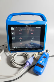 Blue GE Carescape Dinamap VC150 Vital Signs Monitor medical device with screen on a wooden surface, surrounded by cables and equipment.