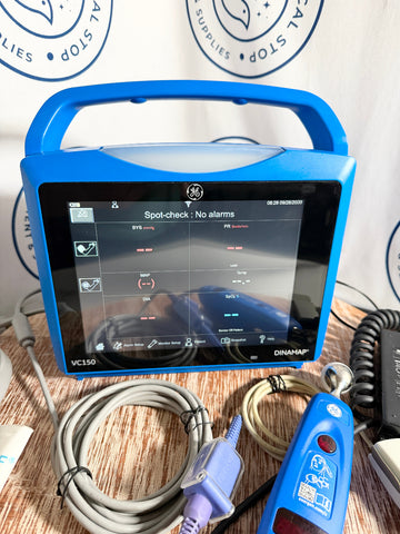 Blue GE Carescape Dinamap VC150 Vital Signs Monitor medical device with screen on a wooden surface, surrounded by cables and equipment.