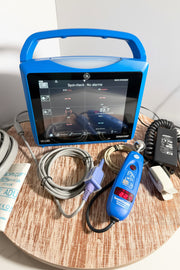 Blue GE Carescape Dinamap VC150 Vital Signs Monitor device with screen on a wooden surface, surrounded by cables and tools.