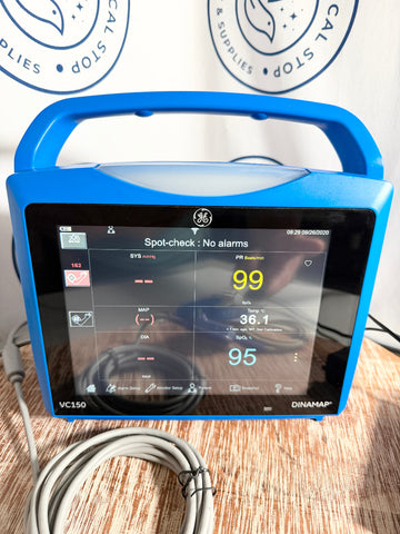 Blue GE Carescape Dinamap VC150 Vital Signs Monitor device with digital display on a wooden surface, branded 'GE' and 'Dinamap'.