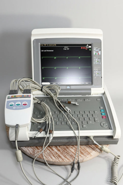 A medical EKG/ECG monitor system with a handheld device, attached wires, a coiled cord, and a small black rectangular accessory.
