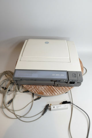 A GE MAC 5500 HD medical imaging device in off-white and gray, shown with its power cord and cables on a wooden surface.