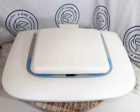 A white GSI AudioStar Ultrasound machine  with a flat rectangular top and curved base, shown on a round wooden surface against a white backdrop.