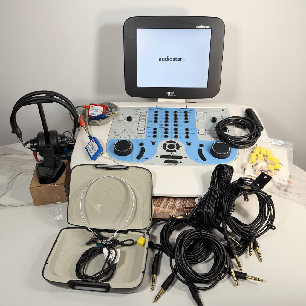 A GSI AudioStar Ultrasound machine  audio mixing console with a built-in monitor screen, shown with its accessories including a microphone, multiple cables, a carrying case, and earplugs on a white marble surface against a branded backdrop.
